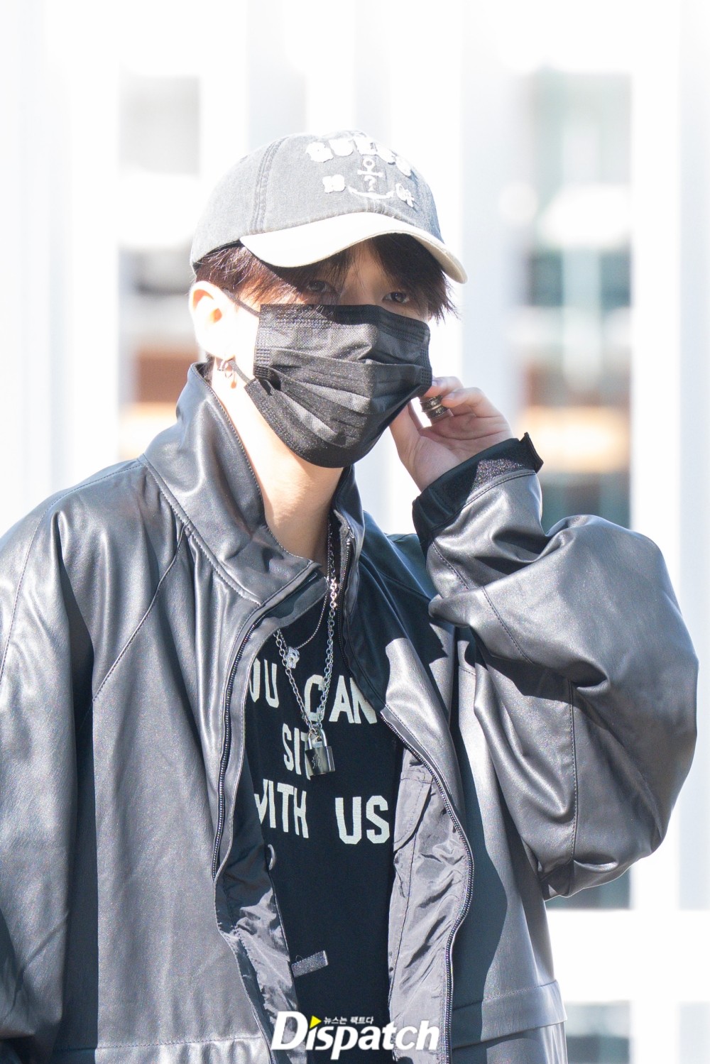 Hyunjin with one hand near his ear, showing his cap and silver jewellery.