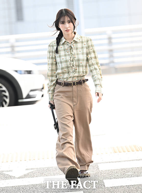 Momo walking in a checked blouse and wide beige trousers.